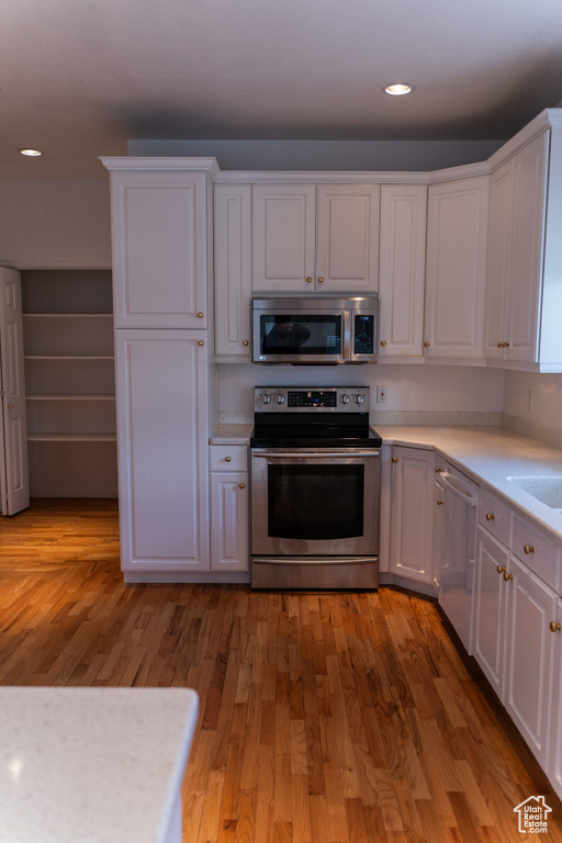 Kitchen with appliances with stainless steel finishes, white cabinetry, light countertops, recessed lighting, and light wood-style flooring