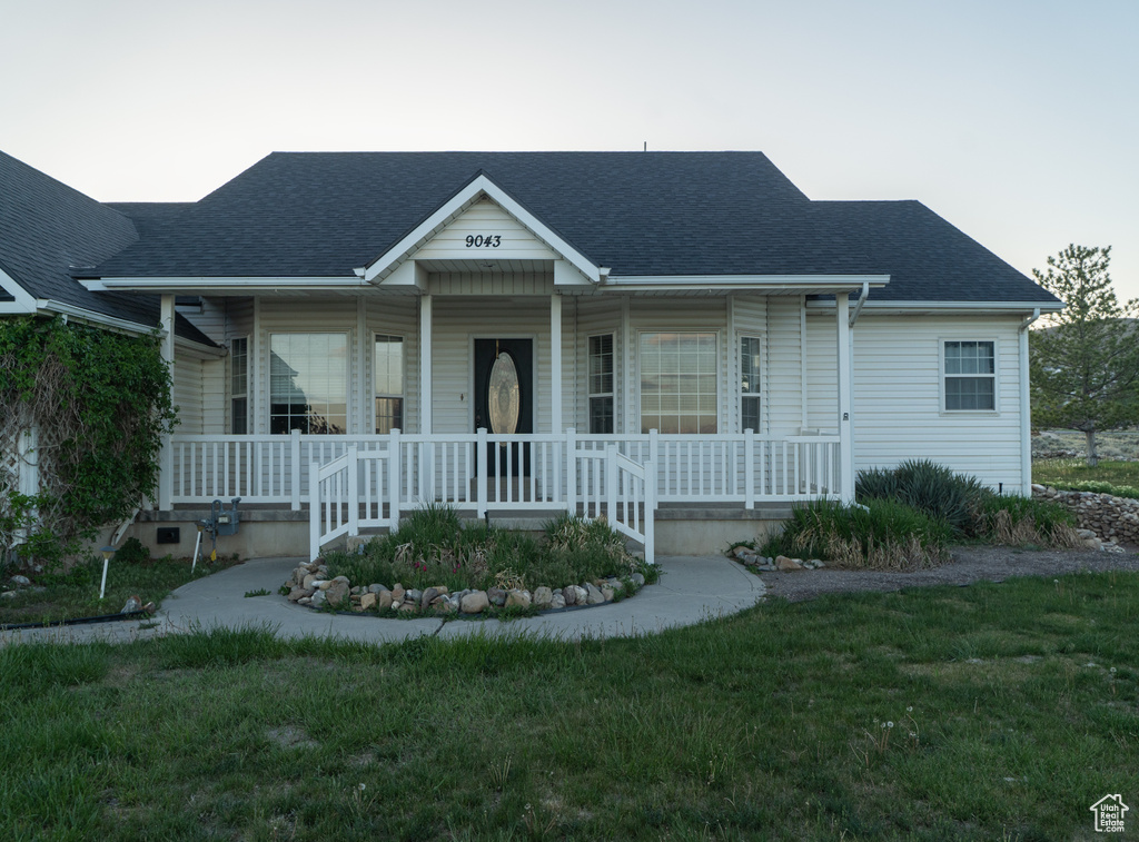 View of front of property featuring a porch, a shingled roof, and a front lawn