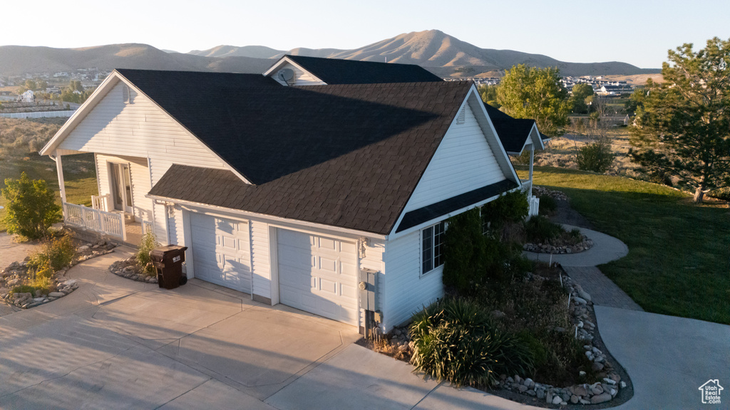 View of property exterior featuring a mountain view, concrete driveway, a yard, an attached garage, and roof with shingles