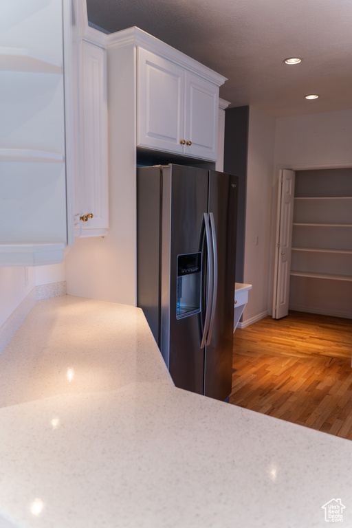 Kitchen featuring stainless steel fridge with ice dispenser, white cabinetry, light wood-type flooring, recessed lighting, and baseboards