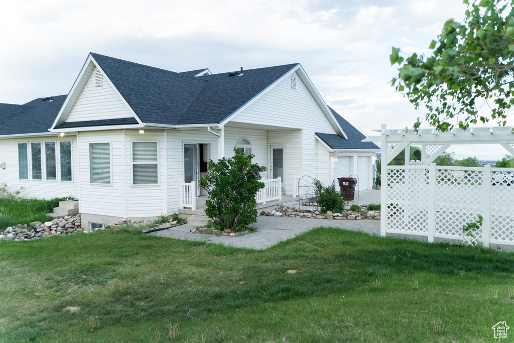 View of front facade with a shingled roof, a porch, a front lawn, and a garage