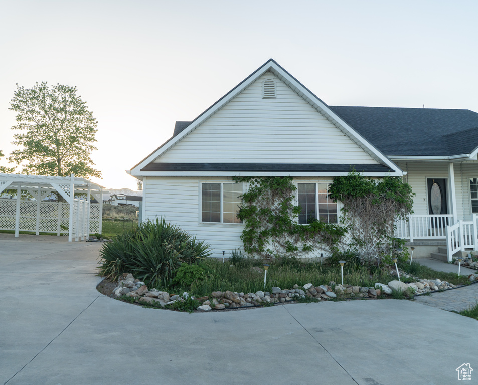 Property exterior at dusk with concrete driveway, a shingled roof, and covered porch