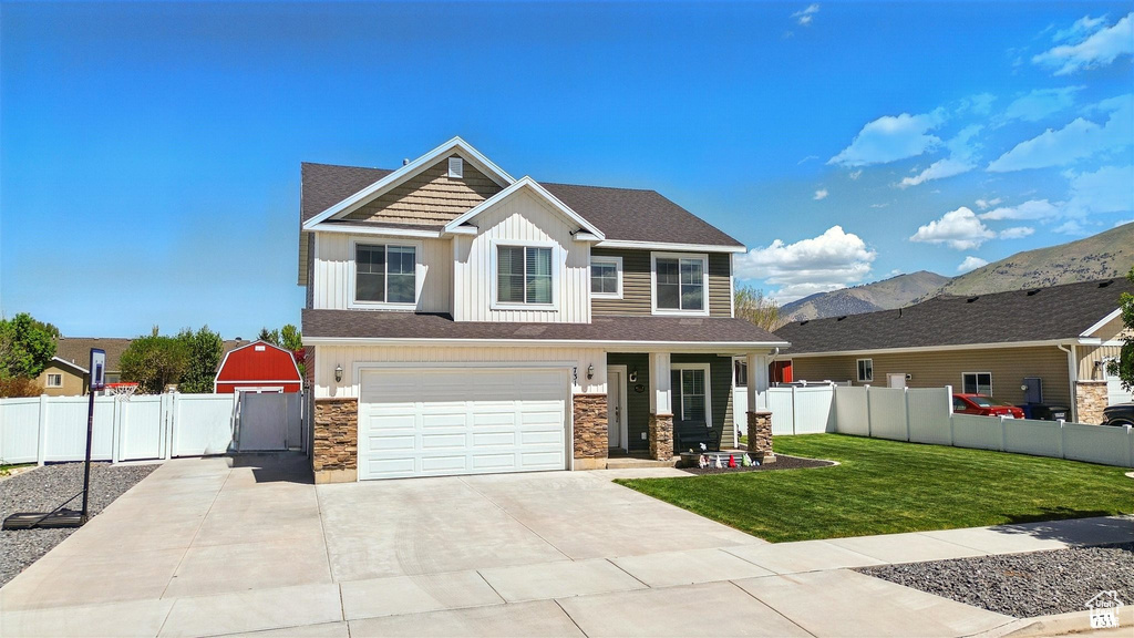 Craftsman-style house featuring stone siding, concrete driveway, an attached garage, board and batten siding, and a gate