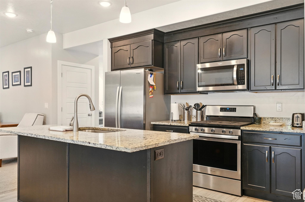 Kitchen with stainless steel appliances, a sink, light stone counters, hanging light fixtures, and recessed lighting