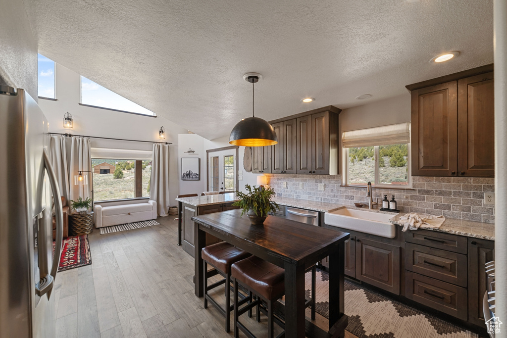 Kitchen featuring a sink, appliances with stainless steel finishes, a textured ceiling, a peninsula, and tasteful backsplash