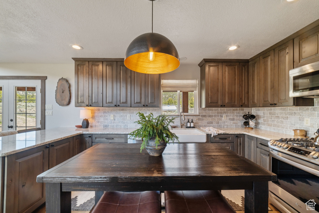 Kitchen with stainless steel appliances, a sink, backsplash, light stone counters, and recessed lighting