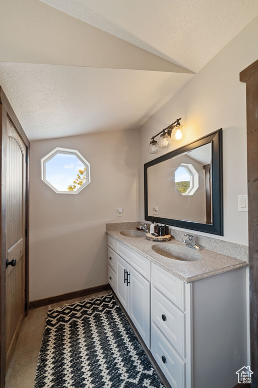 Bathroom featuring double vanity, vaulted ceiling, and a textured ceiling