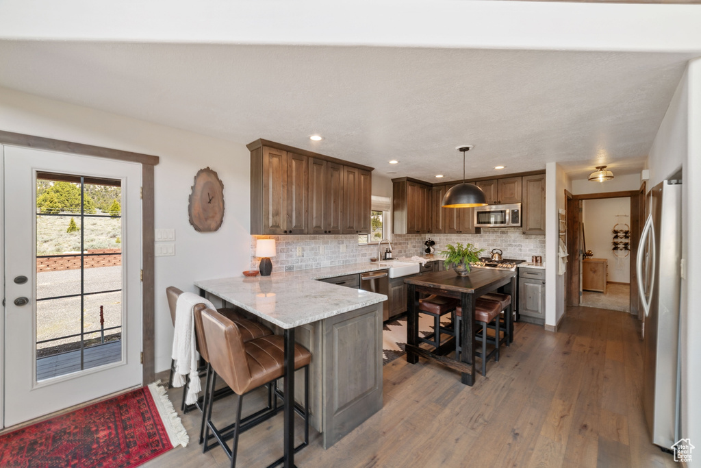 Kitchen with appliances with stainless steel finishes, a peninsula, backsplash, light wood-style flooring, and plenty of natural light