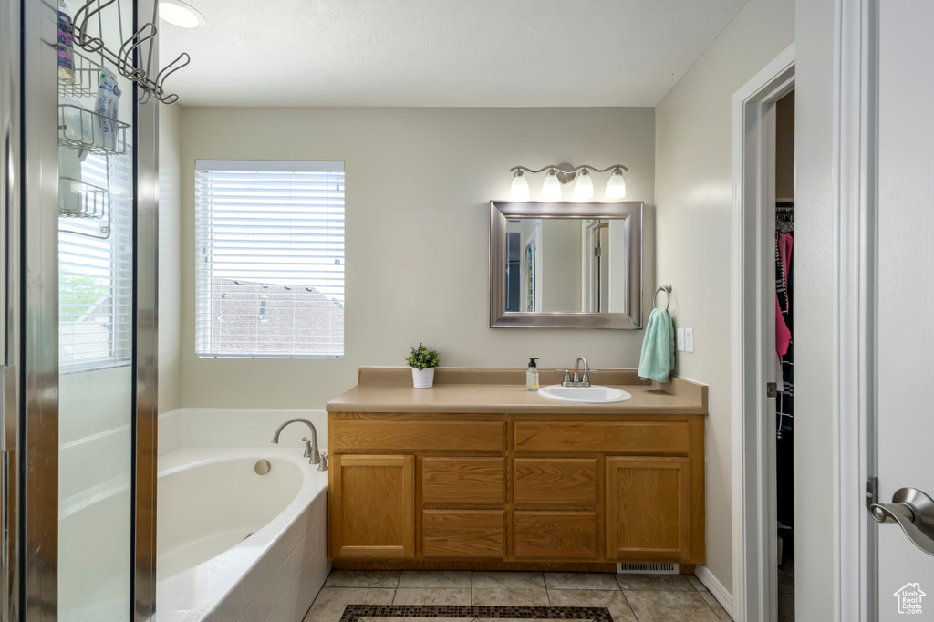 Full bathroom featuring a garden tub, a spacious closet, vanity, and tile patterned flooring