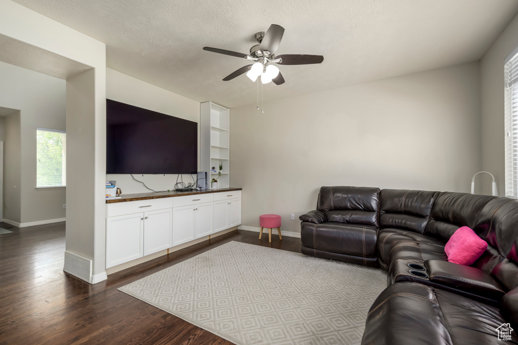 Living room with ceiling fan, dark wood-type flooring, baseboards, and plenty of natural light