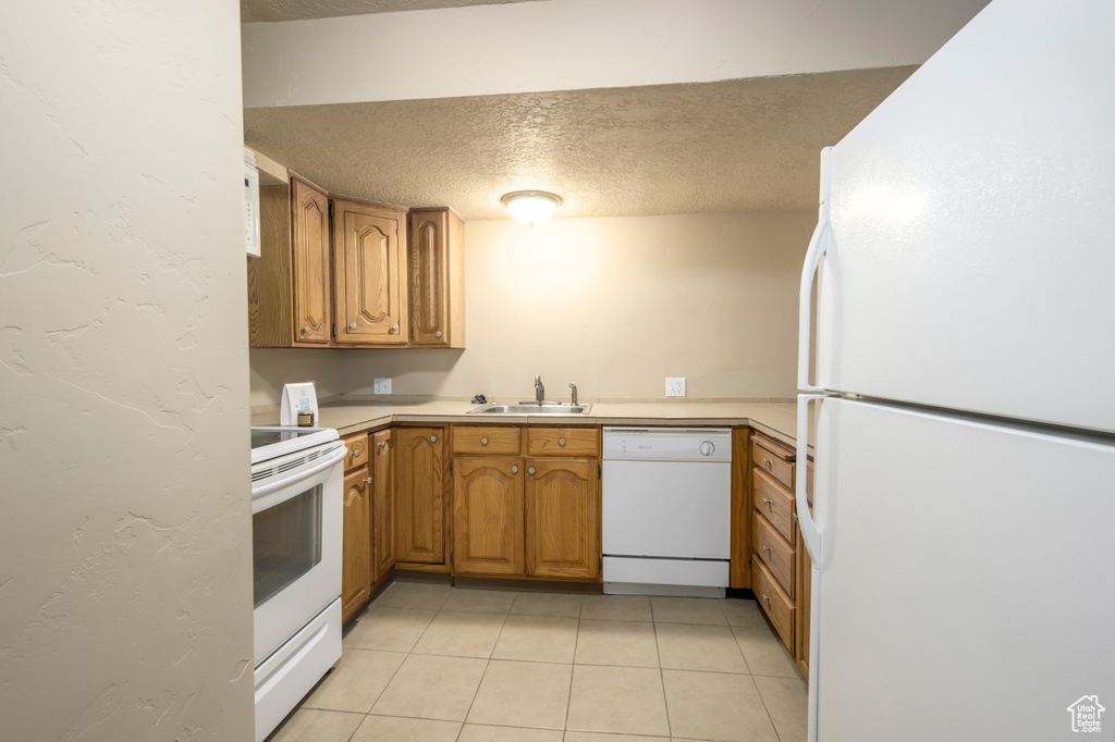 Kitchen featuring white appliances, a textured ceiling, a sink, brown cabinetry, and light countertops