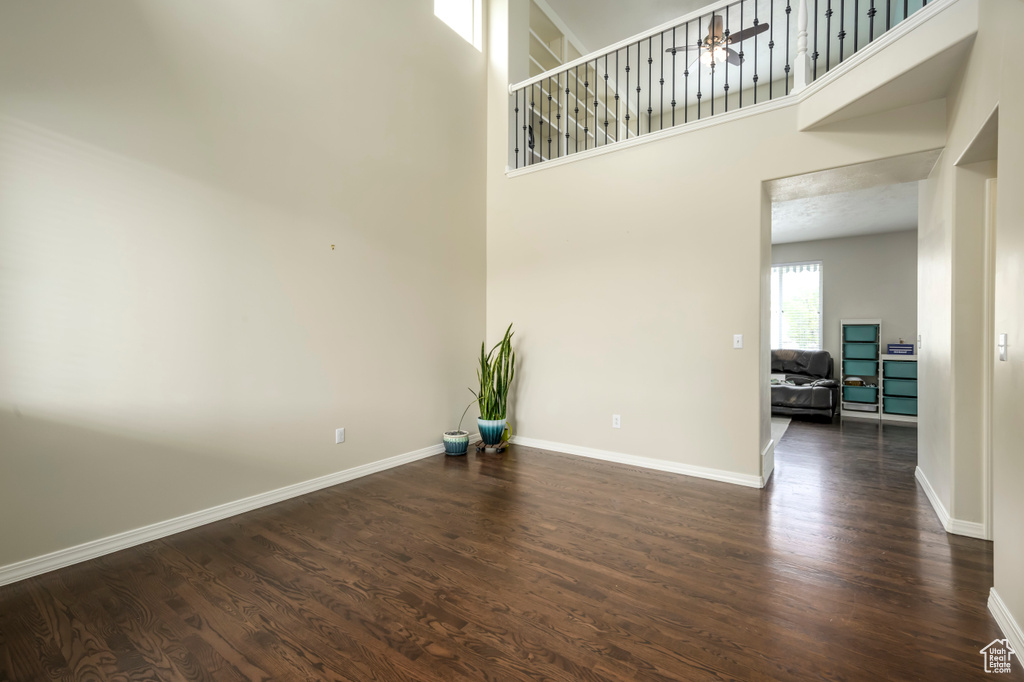 Spare room featuring dark wood-style floors, a ceiling fan, baseboards, and a towering ceiling