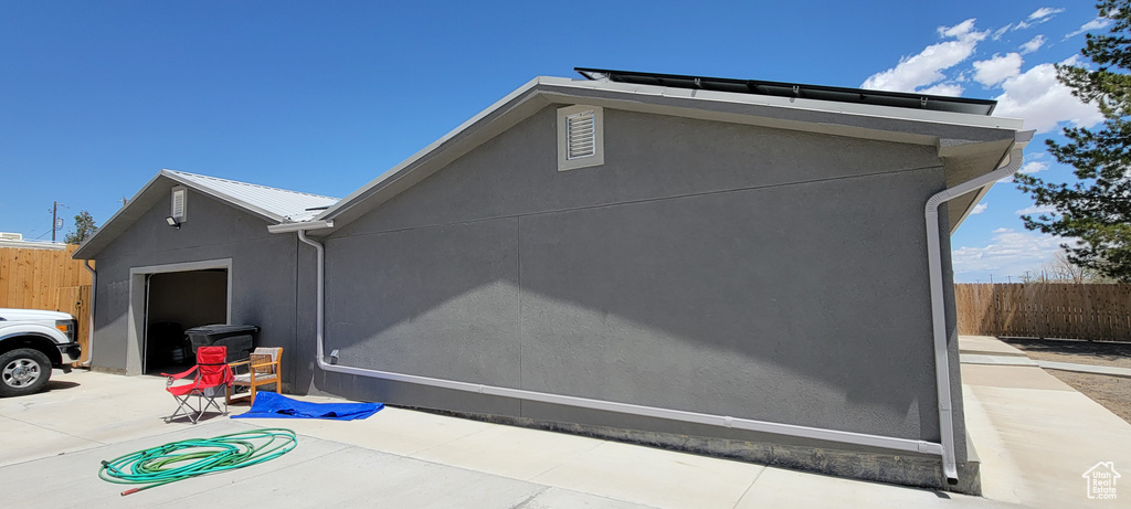 View of property exterior with fence, stucco siding, a patio area, and a garage