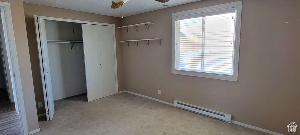 Unfurnished bedroom featuring a baseboard heating unit, a closet, carpet flooring, baseboards, and a textured ceiling