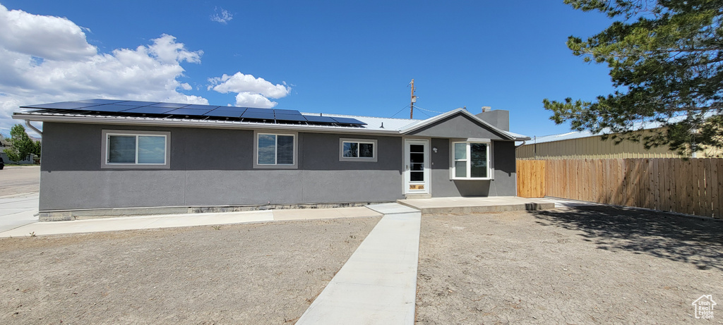 Ranch-style house with stucco siding, fence, solar panels, and a chimney