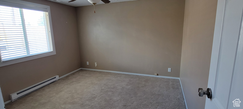 Carpeted spare room featuring a baseboard heating unit, a ceiling fan, plenty of natural light, and baseboards