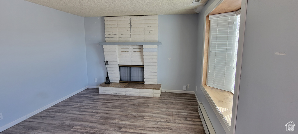 Unfurnished living room with a baseboard heating unit, a textured ceiling, wood finished floors, a brick fireplace, and baseboards