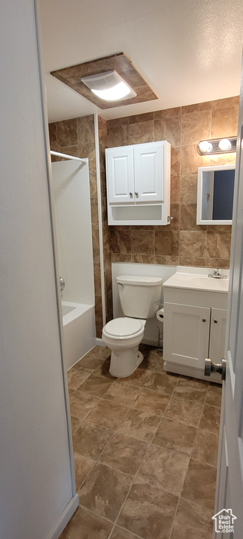 Full bathroom featuring toilet, vanity, bathtub / shower combination, and tile walls