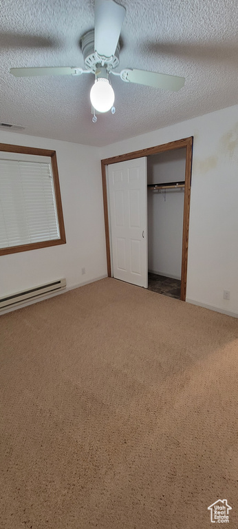 Unfurnished bedroom with carpet, baseboard heating, a closet, a textured ceiling, and a ceiling fan