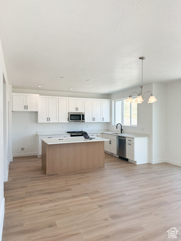Kitchen with stainless steel appliances, a sink, a chandelier, a kitchen island, and light wood-type flooring