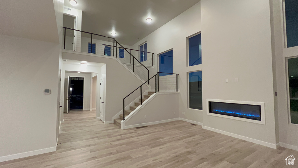 Unfurnished living room with wood finished floors, stairs, a towering ceiling, a glass covered fireplace, and baseboards