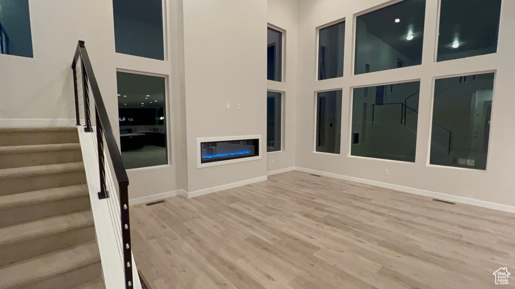 Unfurnished living room featuring a high ceiling, wood finished floors, stairway, and baseboards