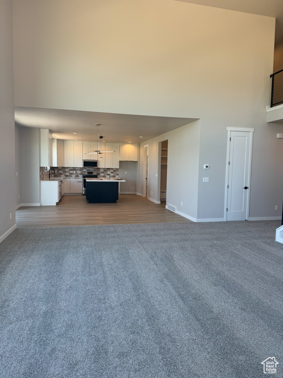 Unfurnished living room featuring light colored carpet, a towering ceiling, and baseboards