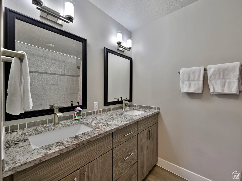 Full bathroom featuring baseboards, wood finished floors, double vanity, tiled shower, and a textured ceiling