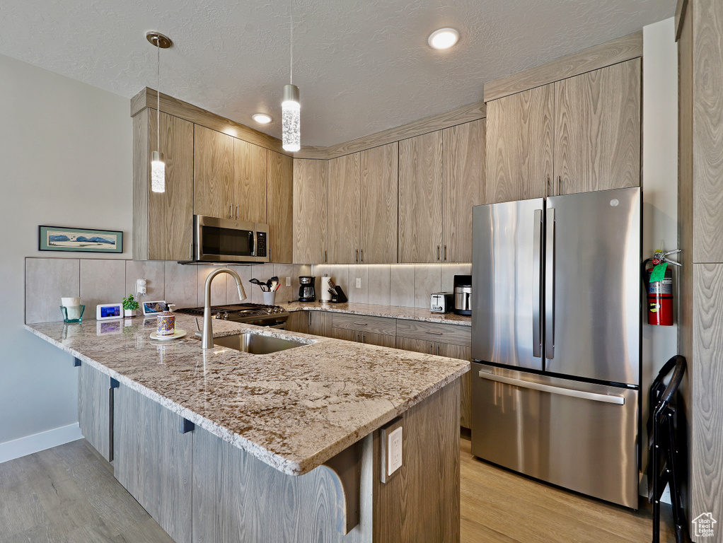 Kitchen featuring appliances with stainless steel finishes, a peninsula, a kitchen bar, light wood-style floors, and decorative backsplash