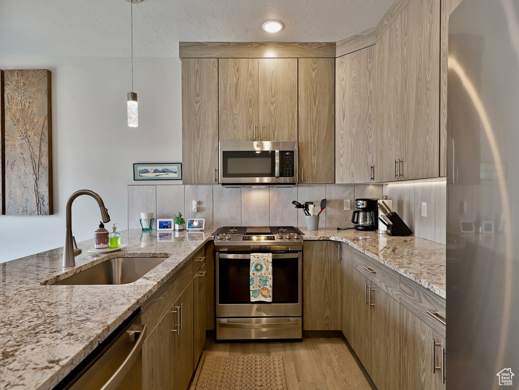 Kitchen featuring stainless steel appliances, a sink, tasteful backsplash, light stone countertops, and light wood-style flooring