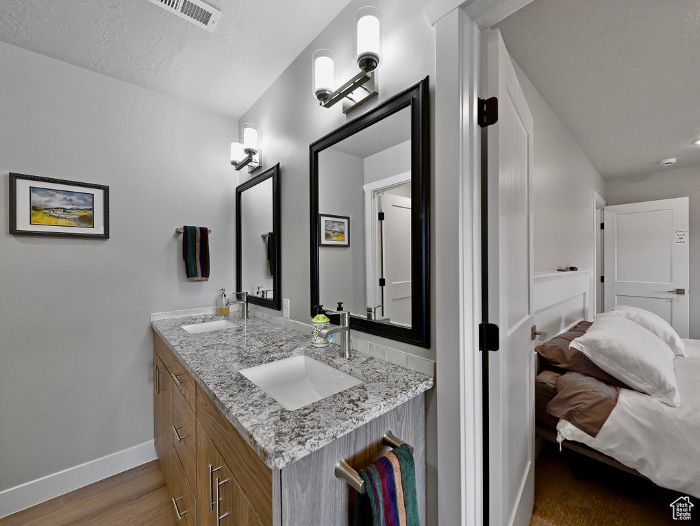 Ensuite bathroom featuring baseboards, double vanity, and wood finished floors