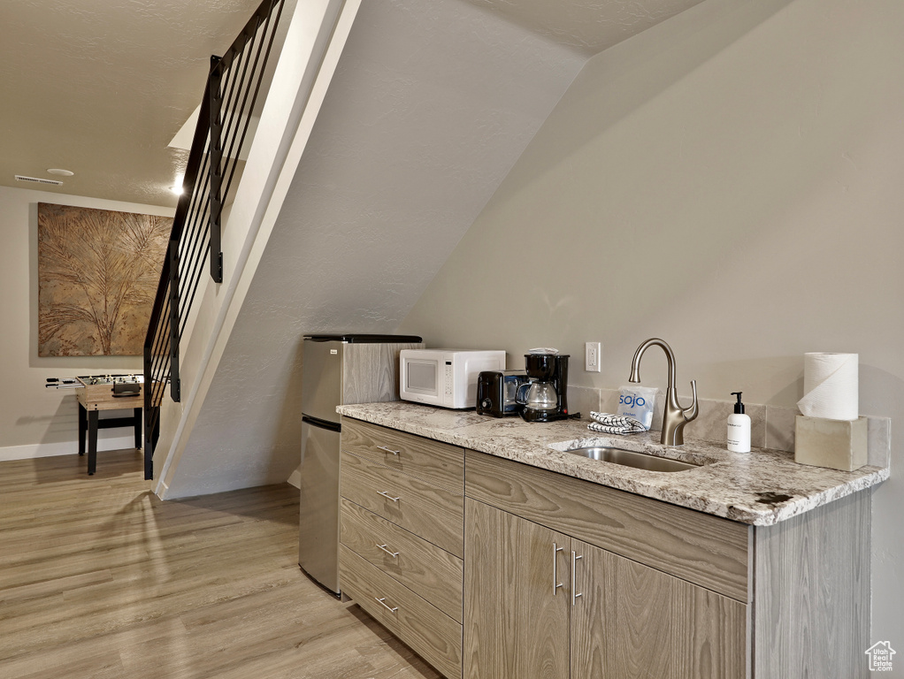 Bar featuring a sink, white microwave, light wood-style flooring, and baseboards