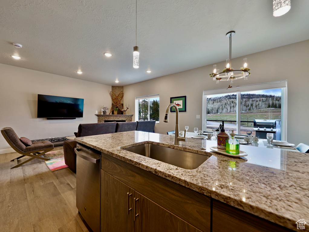 Kitchen featuring a sink, stainless steel dishwasher, decorative light fixtures, a fireplace, and open floor plan