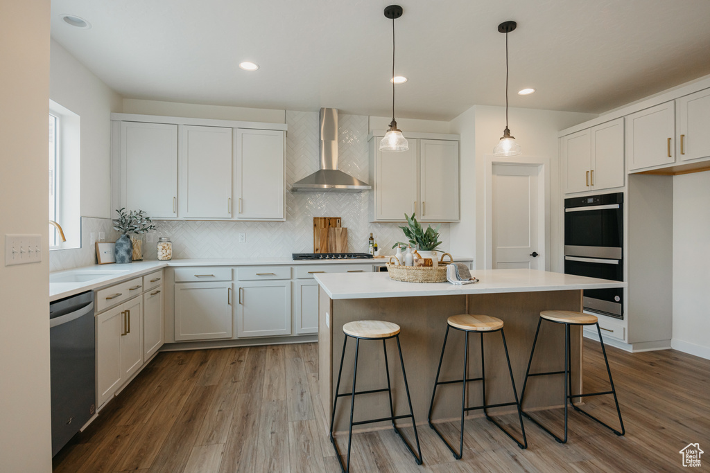 Kitchen with wall chimney exhaust hood, multiple ovens, a kitchen island, a breakfast bar area, and wood finished floors