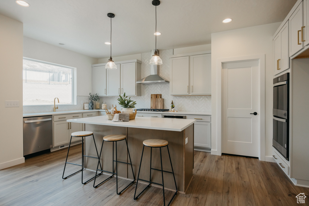 Kitchen featuring appliances with stainless steel finishes, wall chimney exhaust hood, a kitchen bar, a kitchen island, and wood finished floors