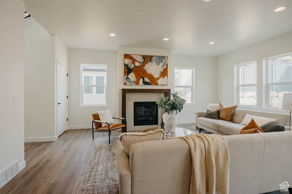 Living room with plenty of natural light, wood finished floors, a glass covered fireplace, recessed lighting, and baseboards