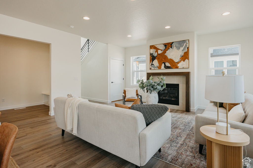Living room with wood finished floors, recessed lighting, baseboards, a tiled fireplace, and stairway