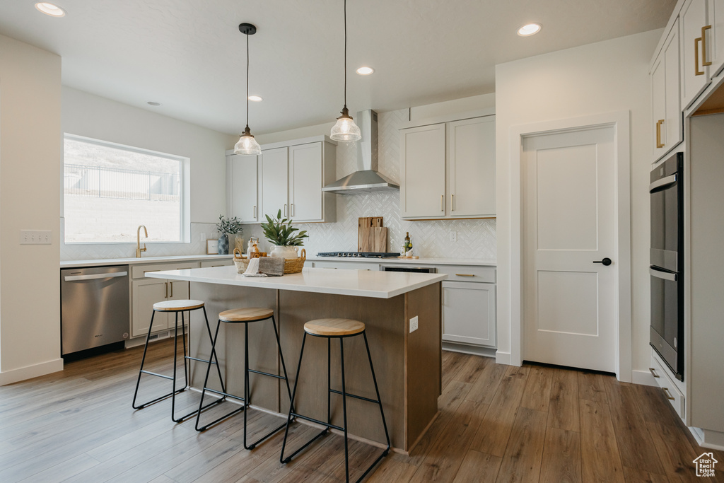 Kitchen with stainless steel dishwasher, wall chimney exhaust hood, a kitchen breakfast bar, light wood-type flooring, and a kitchen island