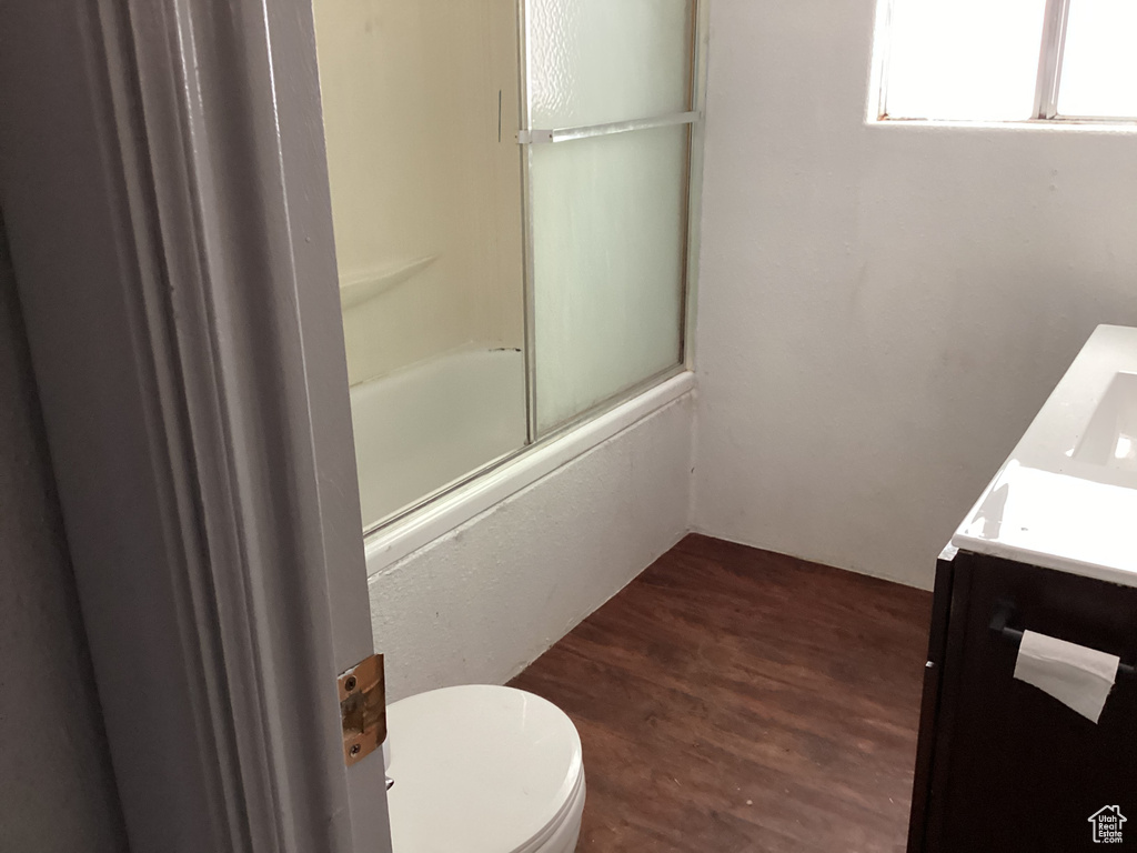 Full bathroom with toilet, wood finished floors, vanity, and bath / shower combo with glass door