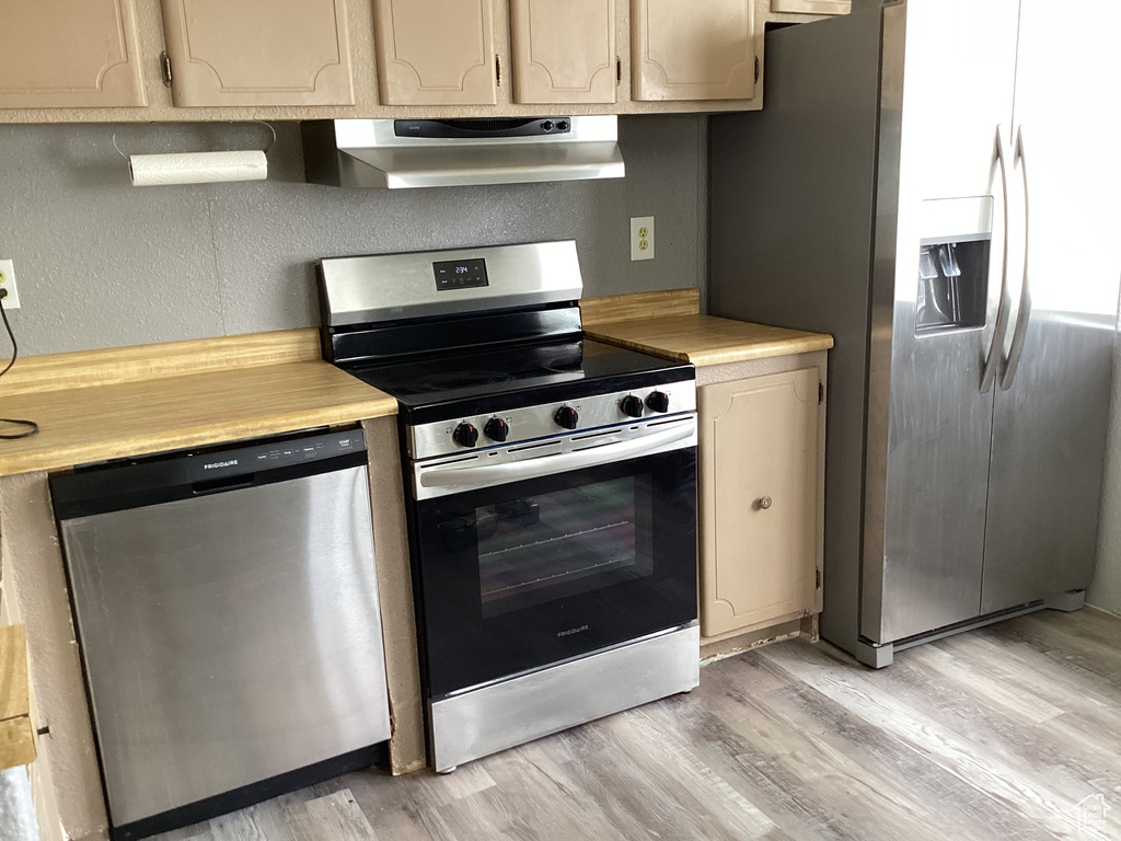 Kitchen featuring stainless steel appliances, ventilation hood, light countertops, and light wood-style flooring