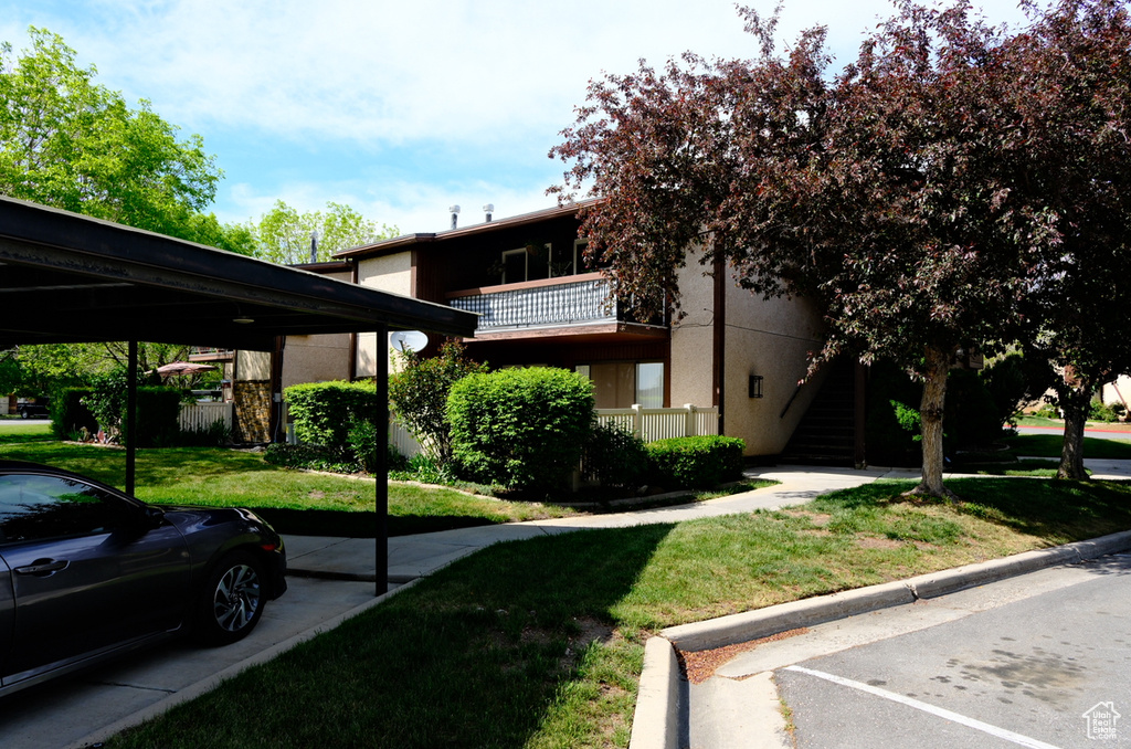 View of front facade with stucco siding, a front lawn, parking, and stairs