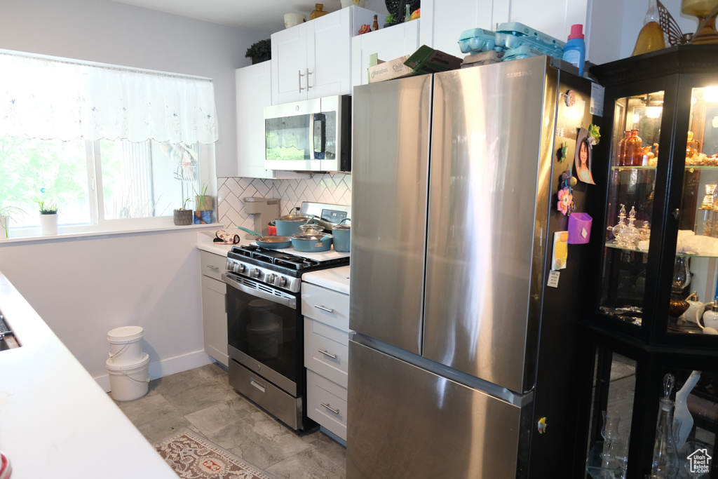 Kitchen featuring stainless steel appliances, decorative backsplash, light countertops, and white cabinetry