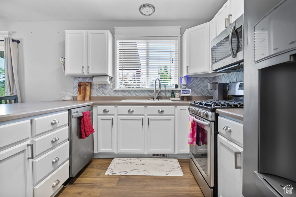 Kitchen featuring appliances with stainless steel finishes, a sink, white cabinets, backsplash, and light countertops