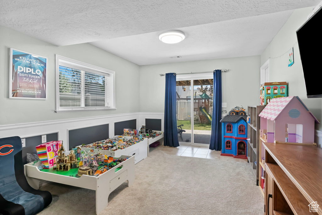 Recreation room featuring carpet, a textured ceiling, and wainscoting