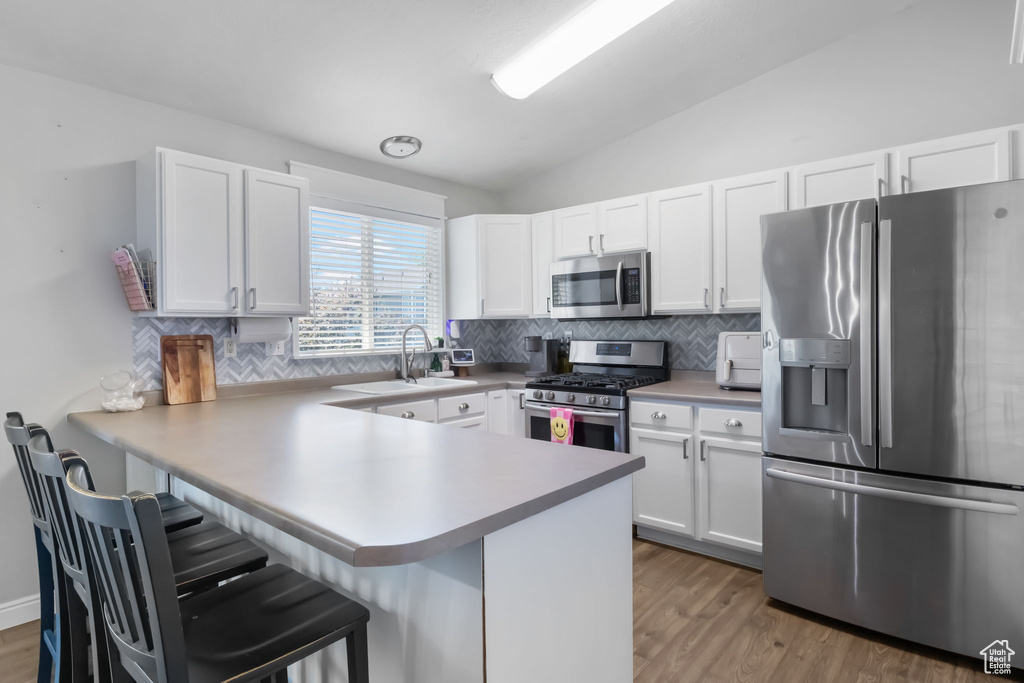 Kitchen featuring stainless steel appliances, a sink, tasteful backsplash, a breakfast bar area, and lofted ceiling