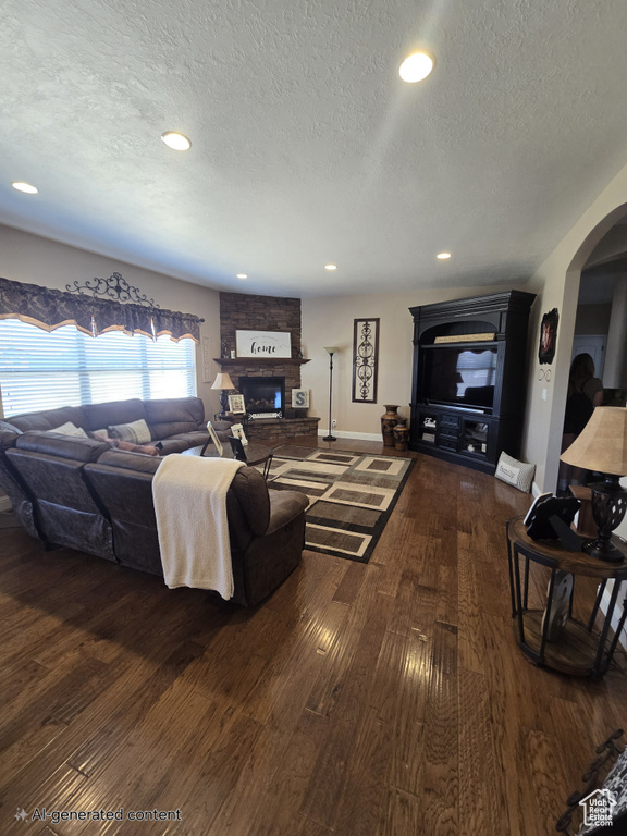 Living room with a stone fireplace, a textured ceiling, dark wood-style flooring, arched walkways, and recessed lighting