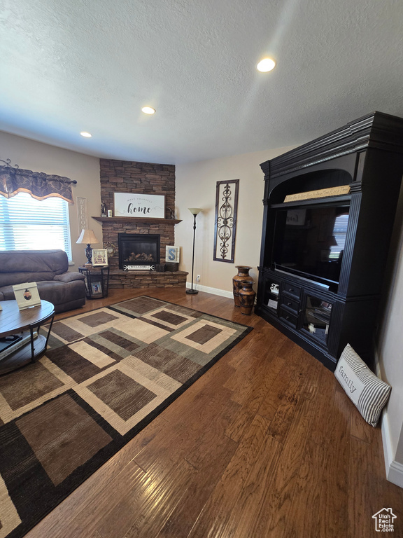 Living room featuring a textured ceiling, wood finished floors, a stone fireplace, recessed lighting, and baseboards