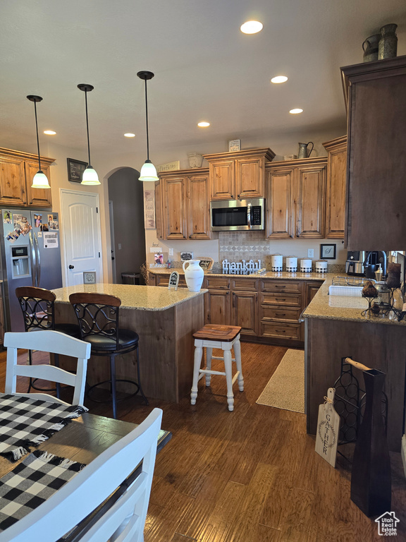 Kitchen featuring stainless steel appliances, arched walkways, dark wood-style flooring, a kitchen breakfast bar, and light stone countertops
