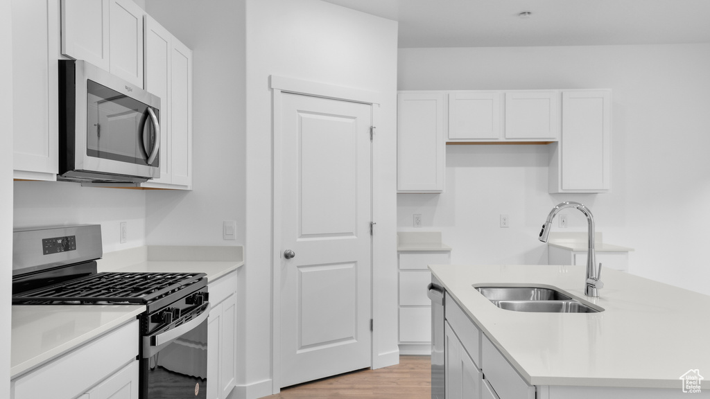 Kitchen featuring stainless steel appliances, a sink, white cabinetry, a center island with sink, and light wood finished floors