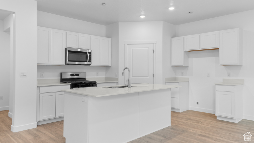 Kitchen with appliances with stainless steel finishes, a sink, a kitchen island with sink, light wood-type flooring, and white cabinetry